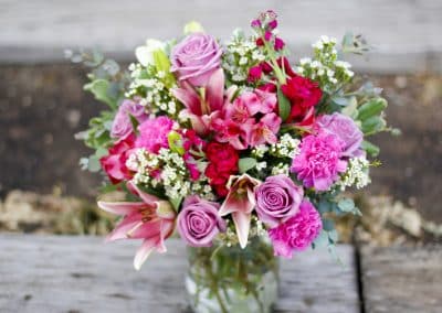 Vased arrangement that includes pink lilies, lavender roses, wax flowers, and eucalyptus.
