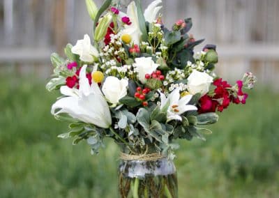 Vased arrangement that includes white lilies, white roses, pink stock, and pink hypericum berries.