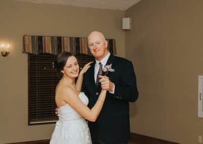 Bride and father dancing. Father is wearing a boutonniere that includes purple roses and silver eucalyptus.
