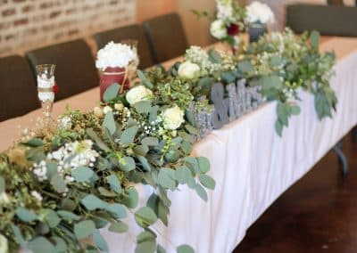Head table greenery garland that includes eucalyptus, baby's breath, and white roses.