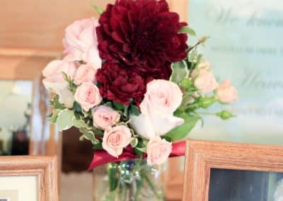 Centerpiece in a mason jar that includes pink roses, burgundy dahlias, and pink mini roses.