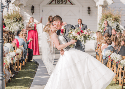 Bride and groom kissing at the end of wedding isle while bride holding her bouquet that has burgundy dahlias, pink mini roses, lisianthus, baby's breath, and eucalyptus.