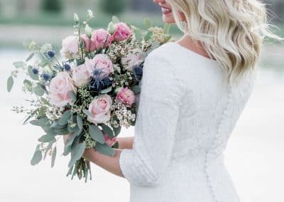 Beautiful bride holding wedding bouquet with pink roses, thistle, and eucalyptus.