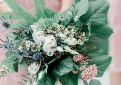 A bridesmaids in a blush pink dress holding her bridesmaid's bouquet that include ivory roses, wax flower, thistle, and eucalyptus, and ferns.