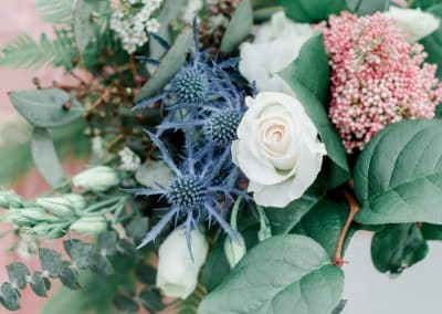 A bridesmaids in a blush pink dress holding her bridesmaid's bouquet that include ivory roses, wax flower, thistle, and eucalyptus, and ferns.