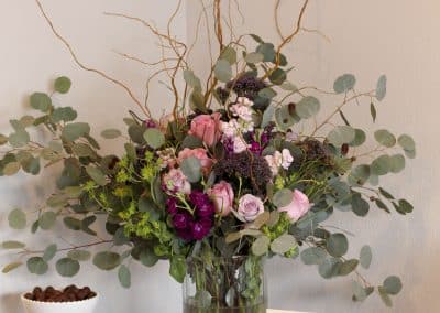 Large arrangement in glass vase with pink roses, curly willow, and eucalyptus.
